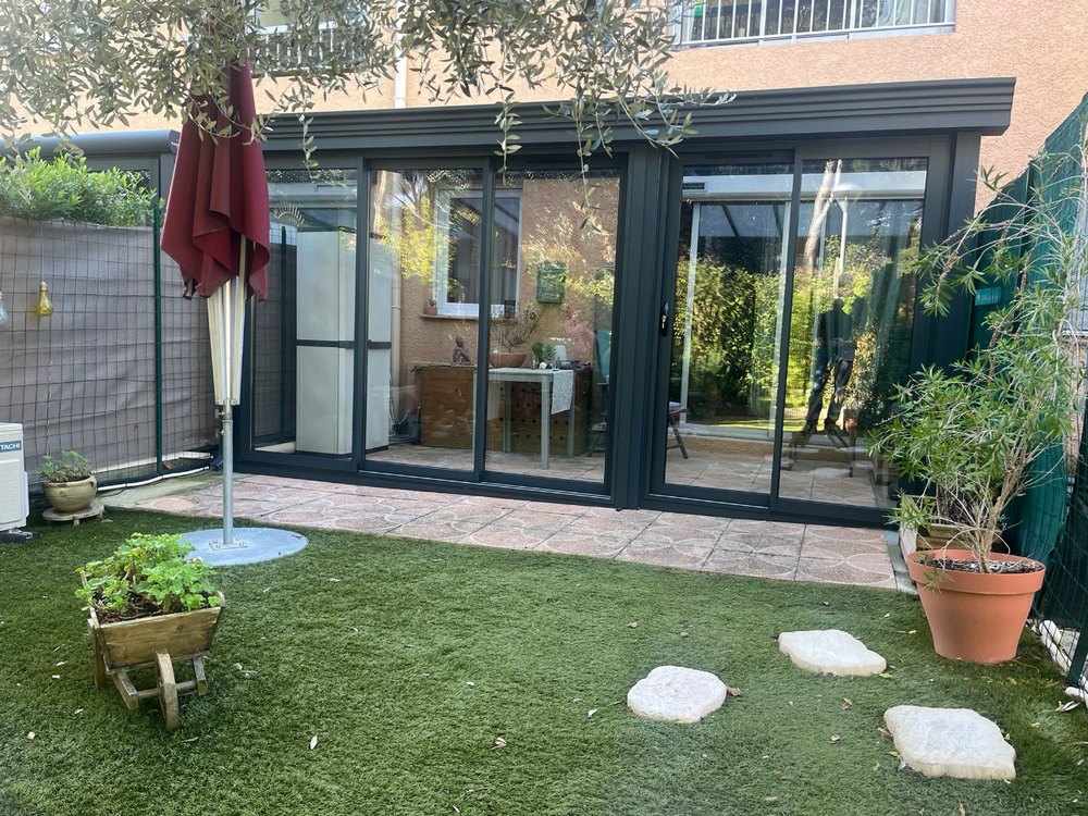 Véranda aluminium gris anthracite à coulissants donnant sur un jardin