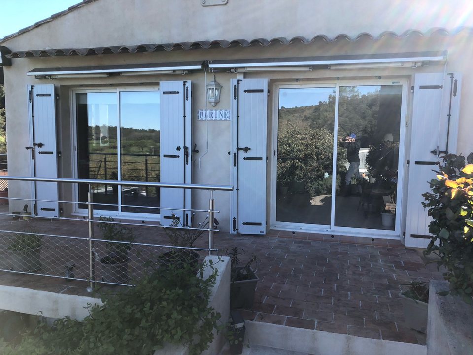 Baies coulissantes aluminium blanc avec volets battants sur une terrasse